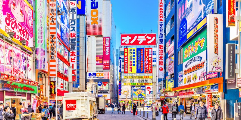 Crowds pass below colorful signs in Akihabara